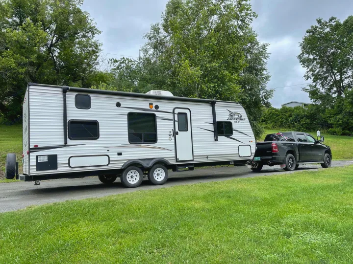 This RV rental travel trailer is ready for adventure, hitched to a black pickup truck on a scenic road.. Jayco Jay Flight SLX 2017
