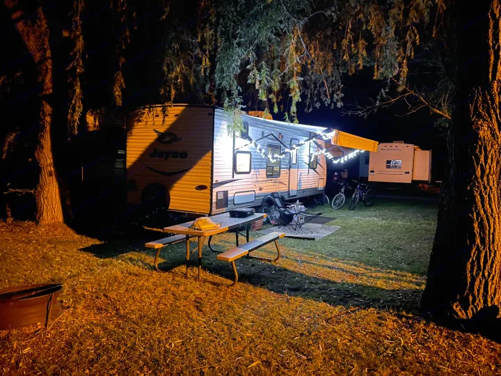 Illuminated Jayco and Wildwood RV rentals at night, adorned with string lights, picnic table, and bikes in a cozy campsite.. Jayco Jay Flight SLX 2017