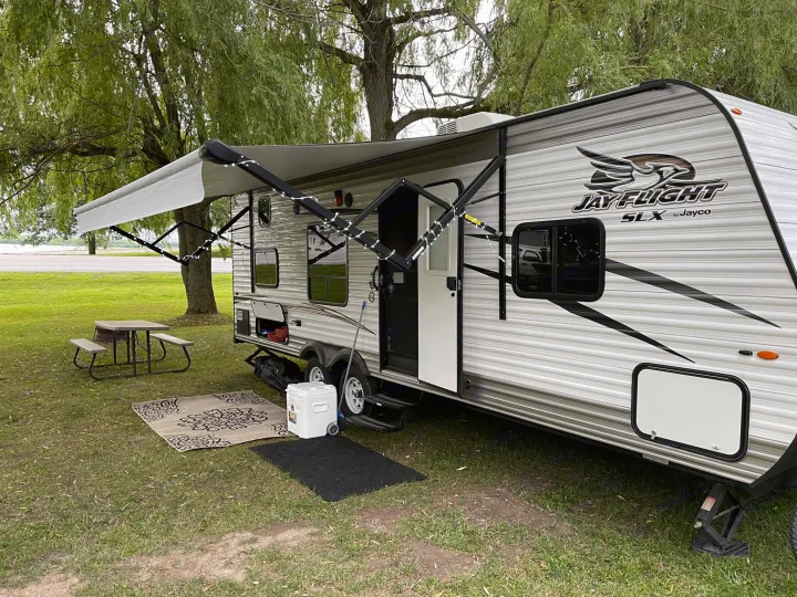 Travel trailer RV rental setup at a scenic campsite with awning, mats, and picnic table for outdoor relaxation.. Jayco Jay Flight SLX 2017