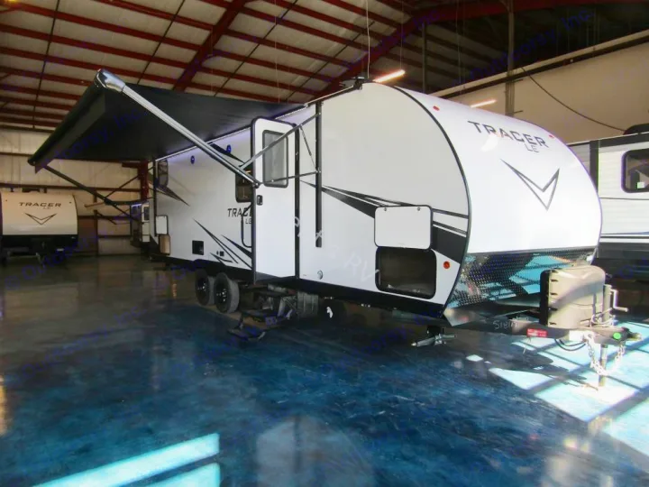 This new white Tracer LE travel trailer, with its extended awning, is perfect for your next rv rental adventure, displayed indoors.. Prime Time RV 260BHSLE 2022