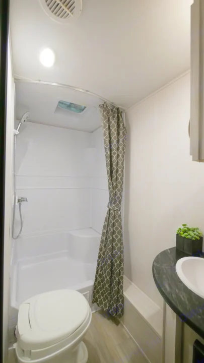Inside a bright RV rental bathroom: compact white shower, toilet, and dark countertop sink. Functional and modern design.. Prime Time RV 260BHSLE 2022
