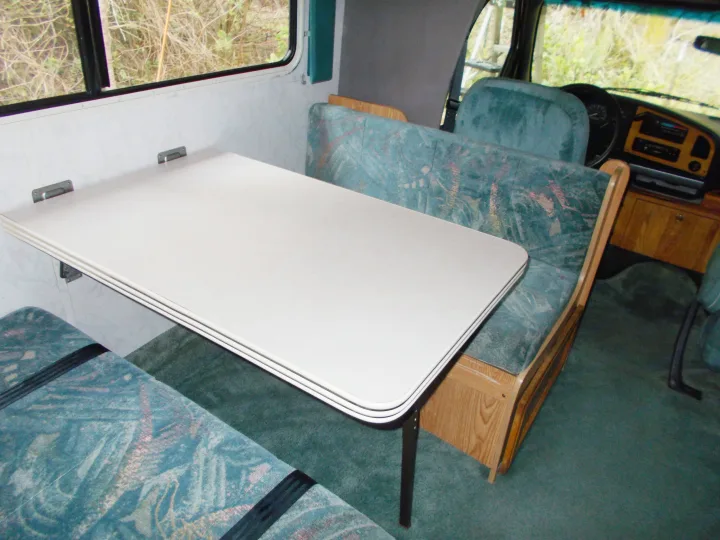 RV rental interior: White table and teal patterned benches with matching carpet create a cozy dining area inside the camper.. Gulf Stream Conquest Lite 1996