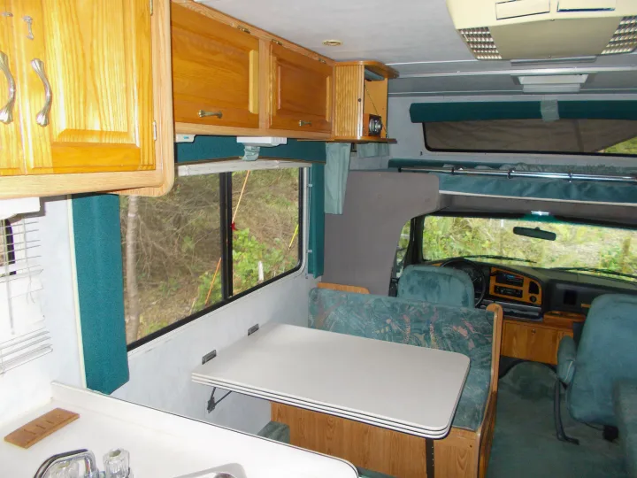 RV rental interior: wood cabinets, a green dinette, kitchen counter, and driver's cab with an over-cab bunk.. Gulf Stream Conquest Lite 1996