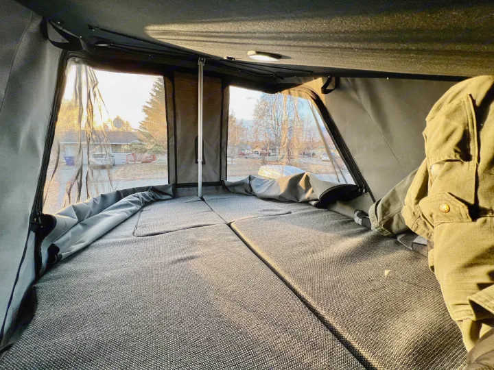 RV rental's cozy rooftop tent interior: A comfortable bed with mesh windows offers neighborhood views. Person relaxes inside.. Honda Element Ecamper 2008