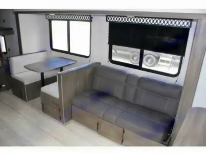 Functional RV rental interior with a light-colored dining booth, a grey sofa, and windows for a bright living space.. Other Other 2021