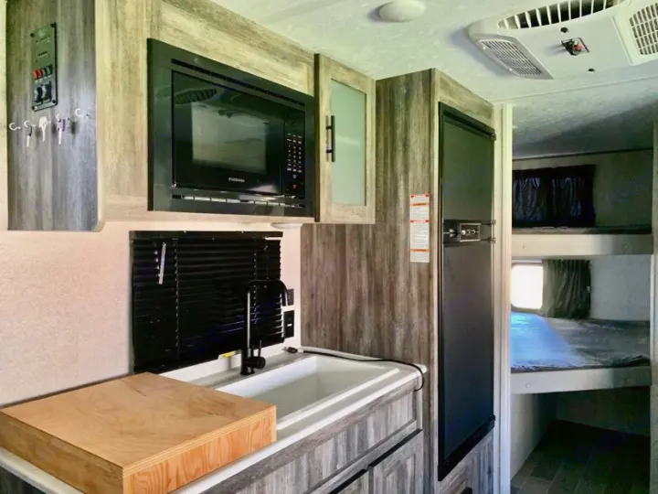 This RV rental interior features a compact kitchen with a microwave, sink, and fridge, plus bunk beds visible in the background.. Forest River Salem FSX PLATINUM 2020