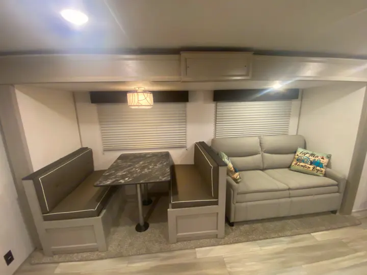 This RV rental features a cozy dinette with booth seating and a table, alongside a comfortable light grey sofa.. Other Tracer 2022