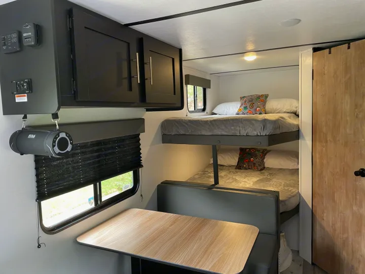An RV rental interior featuring comfortable bunk beds, a dinette table, and dark overhead cabinets. Ready for your next adventure.. Keystone Springdale 2022