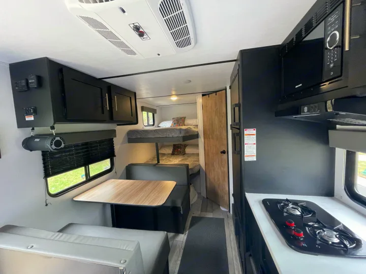 Interior of an RV rental: kitchen with stove and microwave, dining area, and bunk beds visible.. Keystone Springdale 2022