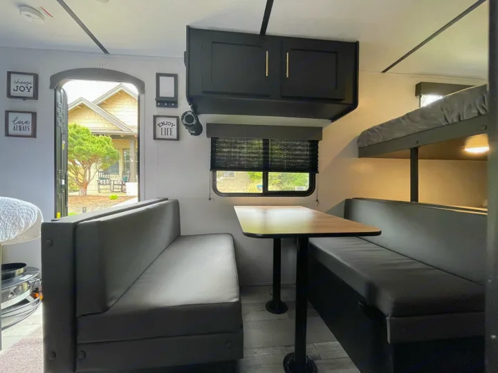 View inside an RV rental, featuring a gray dinette, overhead cabinets, and bunk beds. The door is open to outside.. Keystone Springdale 2022