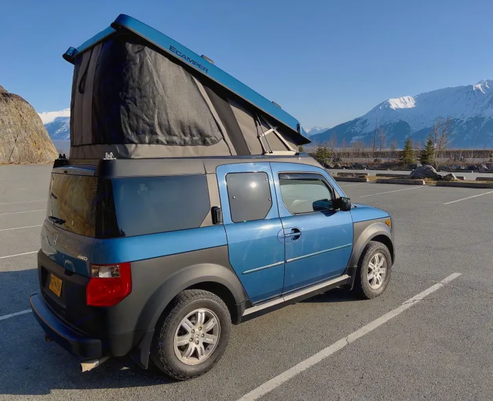 A blue Honda Element, converted into an ECAMPER with a pop-top tent, parked in a scenic lot with snowy mountains. Perfect for an rv rental.. Honda Element Ecamper 2008