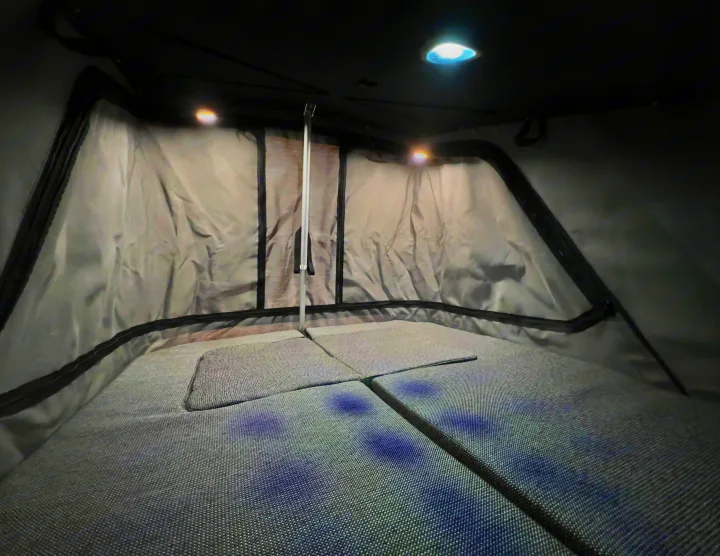Inside an RV rental rooftop tent: a comfortable sleeping area with grey cushions, bright lights, and fabric walls.. Honda Element Ecamper 2008
