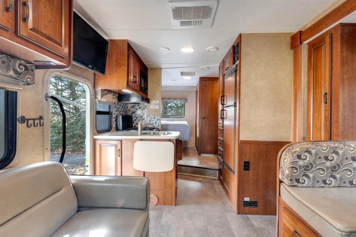 Spacious RV rental interior featuring a full kitchen, comfortable living area with TV, and a glimpse into the rear bedroom.. Forest River Sunseeker 2014