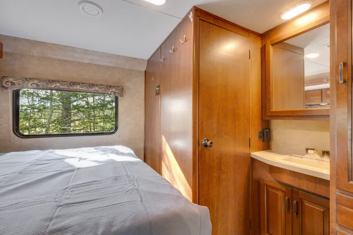 Comfortable RV rental bedroom featuring a bed, window with nature view, and compact vanity. Perfect for your next adventure.. Forest River Sunseeker 2014