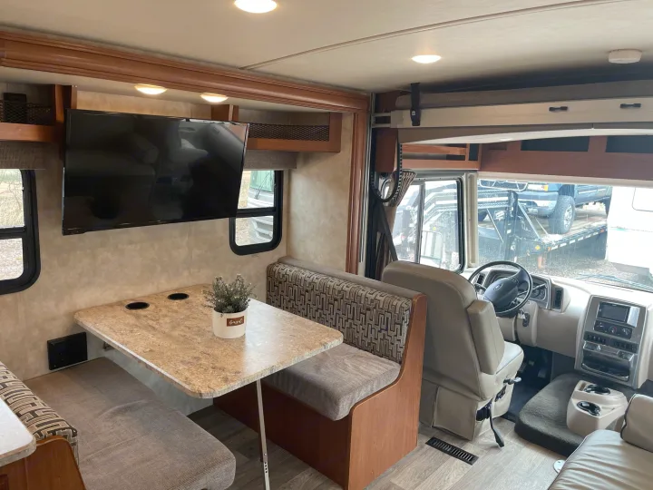 Spacious RV rental interior featuring a dinette with bench seating, wall-mounted TV, and front cockpit area, ideal for travel.. Winnebago Vista 2018
