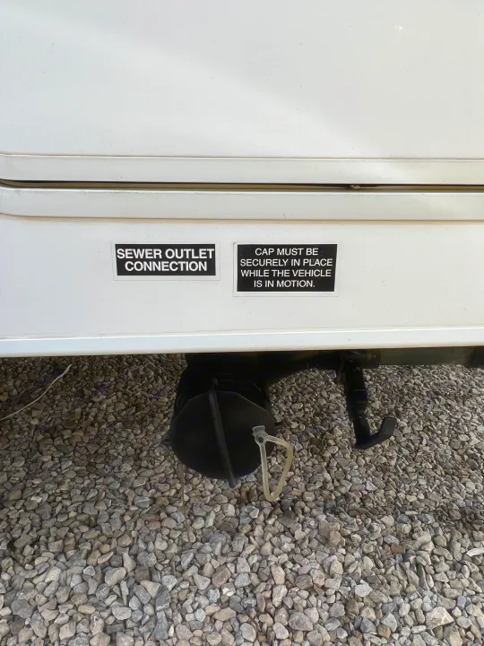 RV rental sewer outlet connection with a warning sticker: "CAP MUST BE SECURELY IN PLACE WHILE THE VEHICLE IS IN MOTION.". Forest River Sunseeker LE 2013