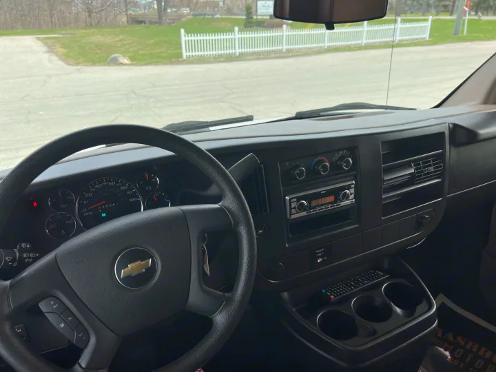Dashboard and steering wheel of a Chevrolet RV rental, with climate controls and a JVC radio visible. View of a road and fence outside.. Forest River Sunseeker LE 2013