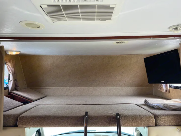 Spacious cab-over bunk bed in an RV rental, featuring a mounted TV, AC, and cozy sleeping area for comfort.. Forest River Sunseeker LE 2013