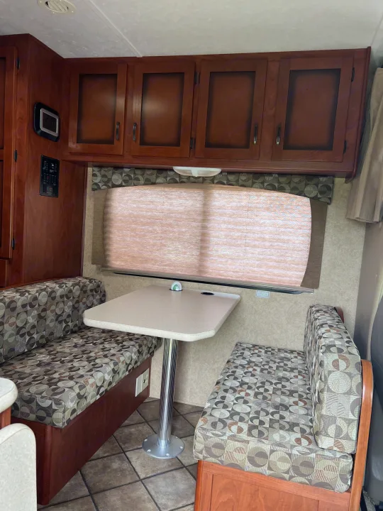 Cozy RV rental dinette with patterned bench seating, a central table, window, and wooden overhead cabinets.. Forest River Sunseeker LE 2013