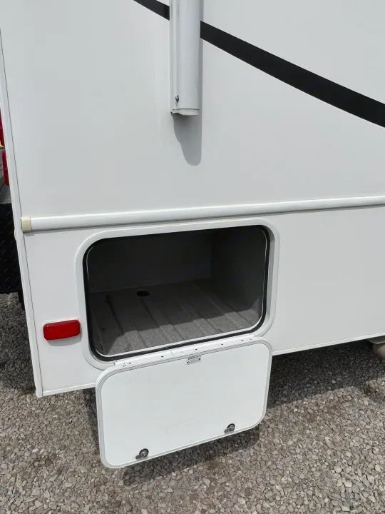 Side view of an RV rental with an open exterior storage compartment on a gravel lot. Good for travel gear.. Forest River Sunseeker LE 2013