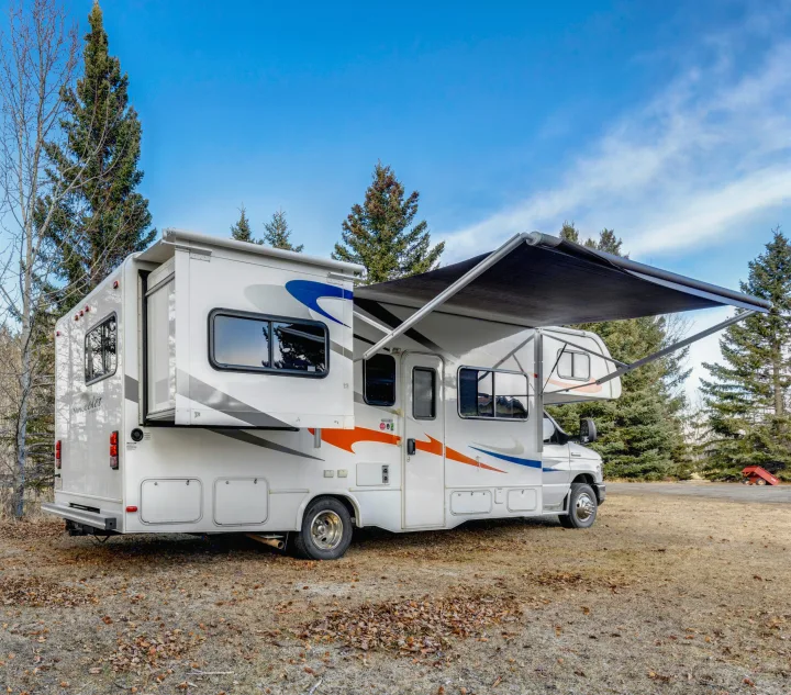 This rv rental, a Class C motorhome with extended awning and slide-out, is parked in a treed, grassy area, perfect for camping.. Forest River Sunseeker 2014