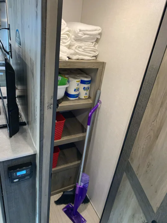 RV rental storage area with shelves, neatly folded towels, toilet paper, cleaning tools, and a solar charge controller.. Forest River Surveyor Legend 296QBLE 2021