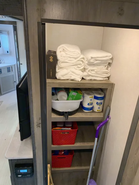 RV rental interior shows organized shelves with fresh towels, cleaning supplies, and toilet paper. Efficient storage for your travels.. Forest River Surveyor Legend 296QBLE 2021
