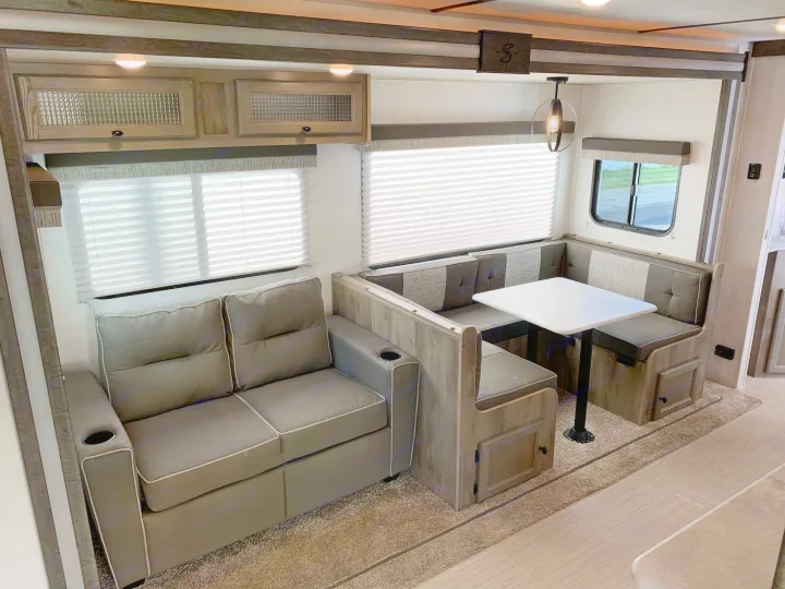 Inside a modern RV rental: cozy living area with a plush sofa, U-shaped dinette, and bright windows. Enjoy your next adventure!. Forest River Surveyor Legend 296QBLE 2021