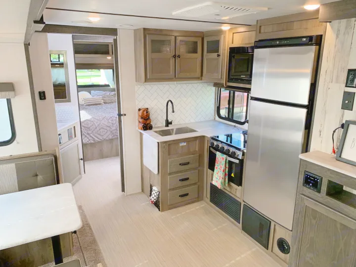 Spacious RV rental interior featuring a modern kitchen with stainless steel appliances, dining booth, and peek into the bedroom. Perfect for travel!. Forest River Surveyor Legend 296QBLE 2021