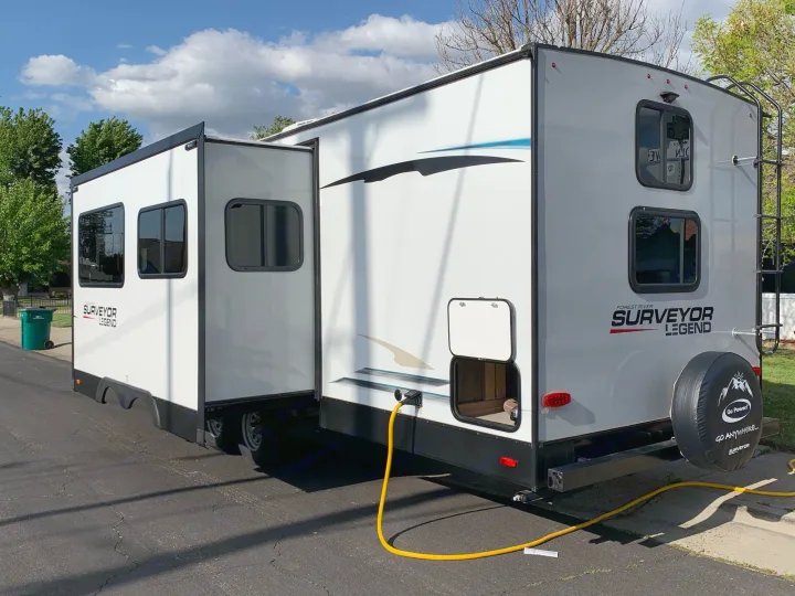 White Surveyor Legend RV rental, a travel trailer with a deployed slide-out, parked on asphalt.. Forest River Surveyor Legend 296QBLE 2021