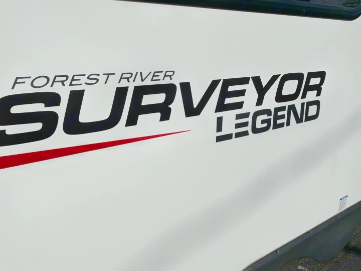 Detail of a white RV rental showing the 'Forest River Surveyor Legend' decal with a red stripe.. Forest River Surveyor Legend 296QBLE 2021