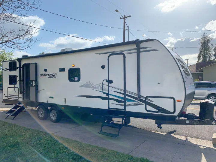 Spacious white travel trailer, a Surveyor Legend RV rental, parked outdoors with steps down.. Forest River Surveyor Legend 296QBLE 2021