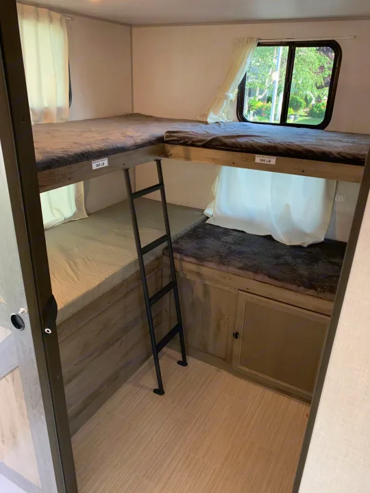 RV rental's L-shaped bunk beds: A compact sleeping area with an upper bunk, lower beds, and a ladder.. Forest River Surveyor Legend 296QBLE 2021