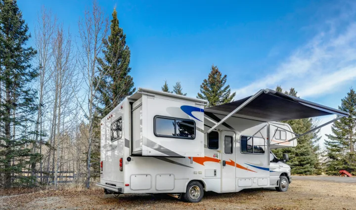Spacious Class C RV rental, a white Sunseeker with an extended awning, parked in a scenic wooded area under a blue sky.. Forest River Sunseeker 2014
