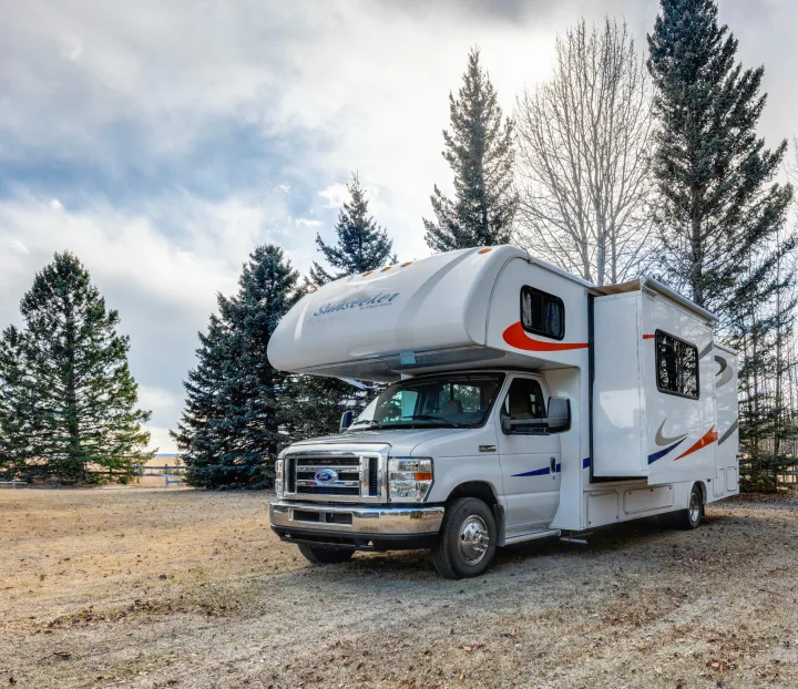 A white Sunseeker RV rental is parked on a dry, grassy field with evergreen trees under a bright, cloudy sky, ready for adventure.. Forest River Sunseeker 2014