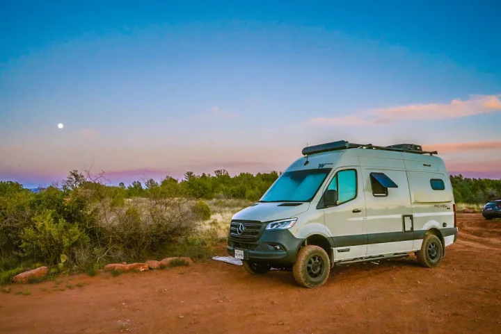 This Winnebago Revel camper van, an ideal rv rental, is parked on a dirt road under a full moon at dusk. Explore off-grid!. Winnebago Revel 2022