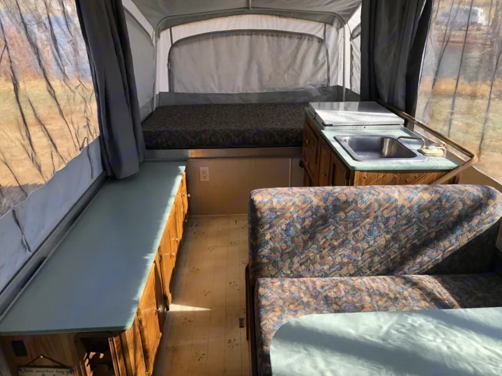 Cozy pop-up camper interior, perfect for rv rental adventures! Features a bed, kitchen, and dinette for camping comfort.. Coleman Chesapeake 1993