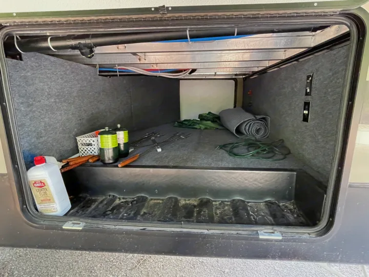 RV rental's basement storage holds camping gear: lighter fluid, propane, grill tools, and a rolled mat.. Forest River Coachmen Chaparral 2017