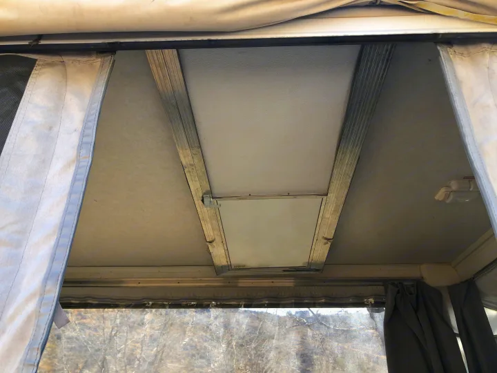 Inside an RV rental pop-up camper: textured ceiling, hinged roof panel, curtains, and window view of outdoor trees.. Coleman Chesapeake 1993