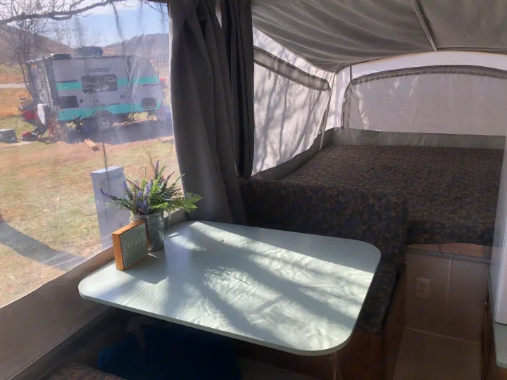 Cozy pop-up RV rental interior featuring a bright table with flowers, comfortable bed, and scenic outdoor view.. Coleman Chesapeake 1993