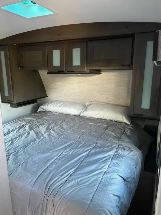 Inside an RV rental bedroom, featuring a comfy bed with grey comforter, white pillows, dark cabinets, and a skylight.. Other Other 2021