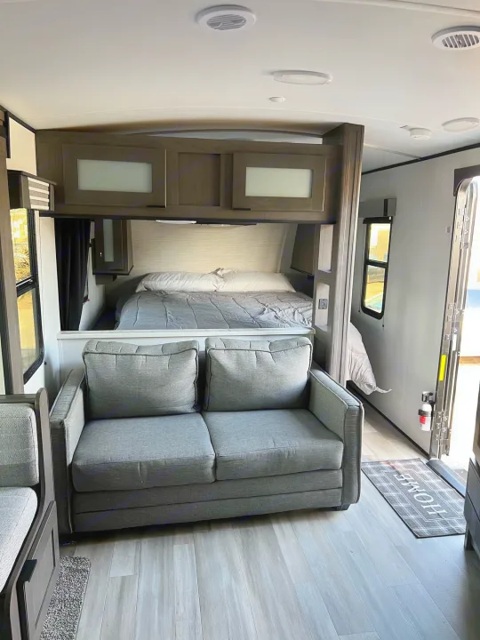 RV rental: bedroom with bed, grey sofa, wood-look flooring, and 'HOME' entry mat.. Other Other 2021