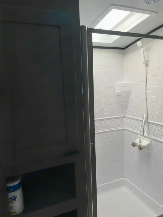 Compact rv rental bathroom: white tiled shower stall with skylight overhead, and dark cabinet storage on the left.. Other Other 2021
