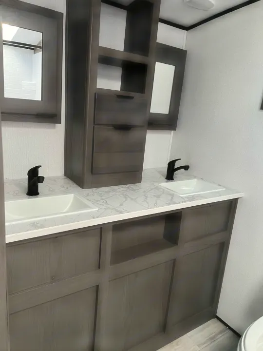 Modern double vanity in an RV rental bathroom, featuring stylish dark cabinetry, marble-look countertop, and sleek black faucets.. Other Other 2021