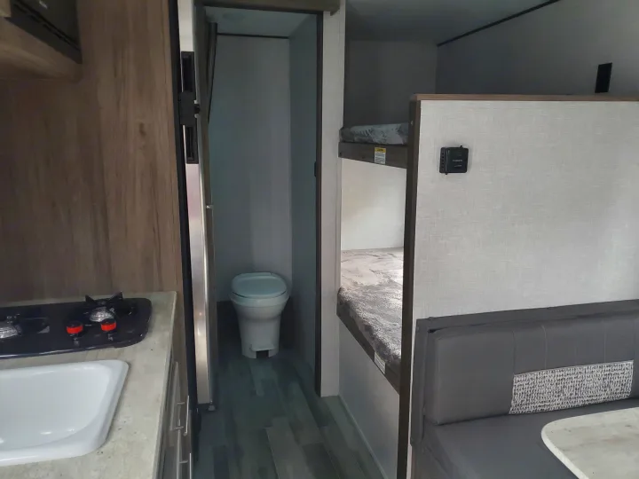 Interior of an RV rental showing kitchenette, bathroom with toilet, bunk beds, and dinette. Ideal for travel adventures.. Crossroads RV Zinger 2021