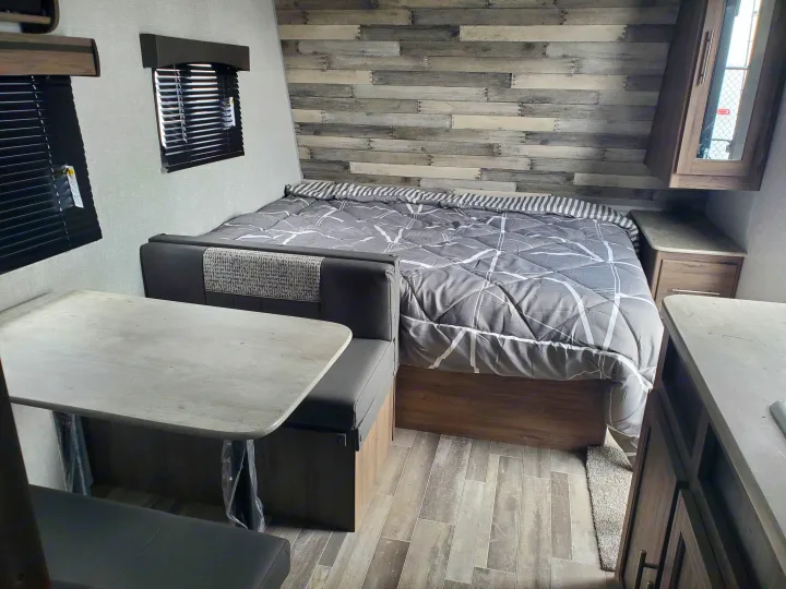 Explore this cozy RV rental interior featuring a large bed, practical dinette with seating, and modern wood-accented walls.. Crossroads RV Zinger 2021