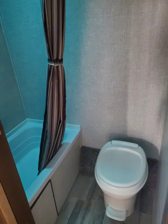 RV rental bathroom: compact white tub/shower, striped curtain, and clean white toilet. Essential amenities for your journey.. Crossroads RV Zinger 2021