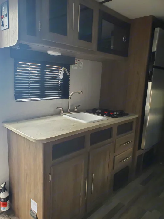 Inside this RV rental, find a compact kitchen with a sink, two-burner stove, microwave, refrigerator, and ample storage.. Crossroads RV Zinger 2021