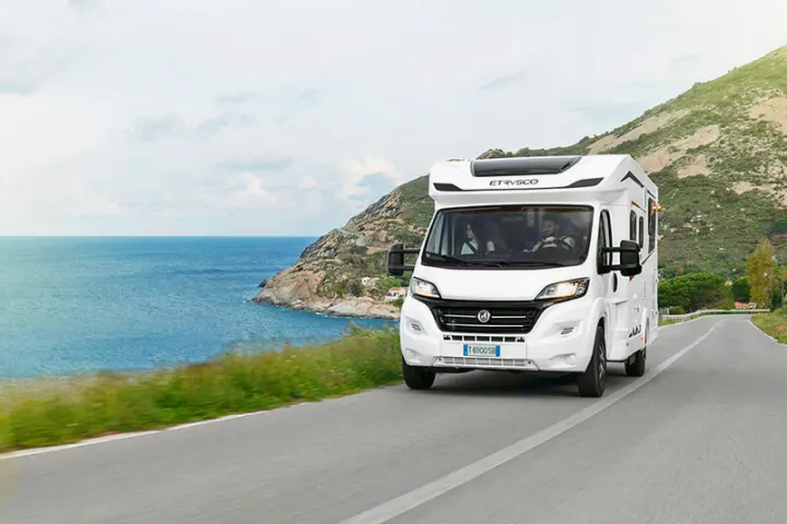 A white motorhome drives along a scenic coastal road with blue ocean and green hills. An ideal RV rental for your next road trip adventure.. Etrusco Etrusco T7400SBC 2021