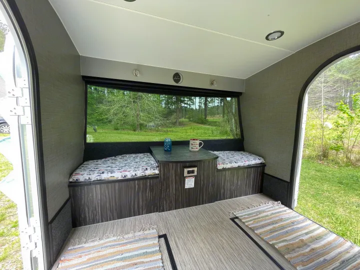 Interior of an RV rental featuring a cozy dinette with cushioned benches, a table, and a large window showcasing a forest view.. InTech RV InTech RV Trailer 2018